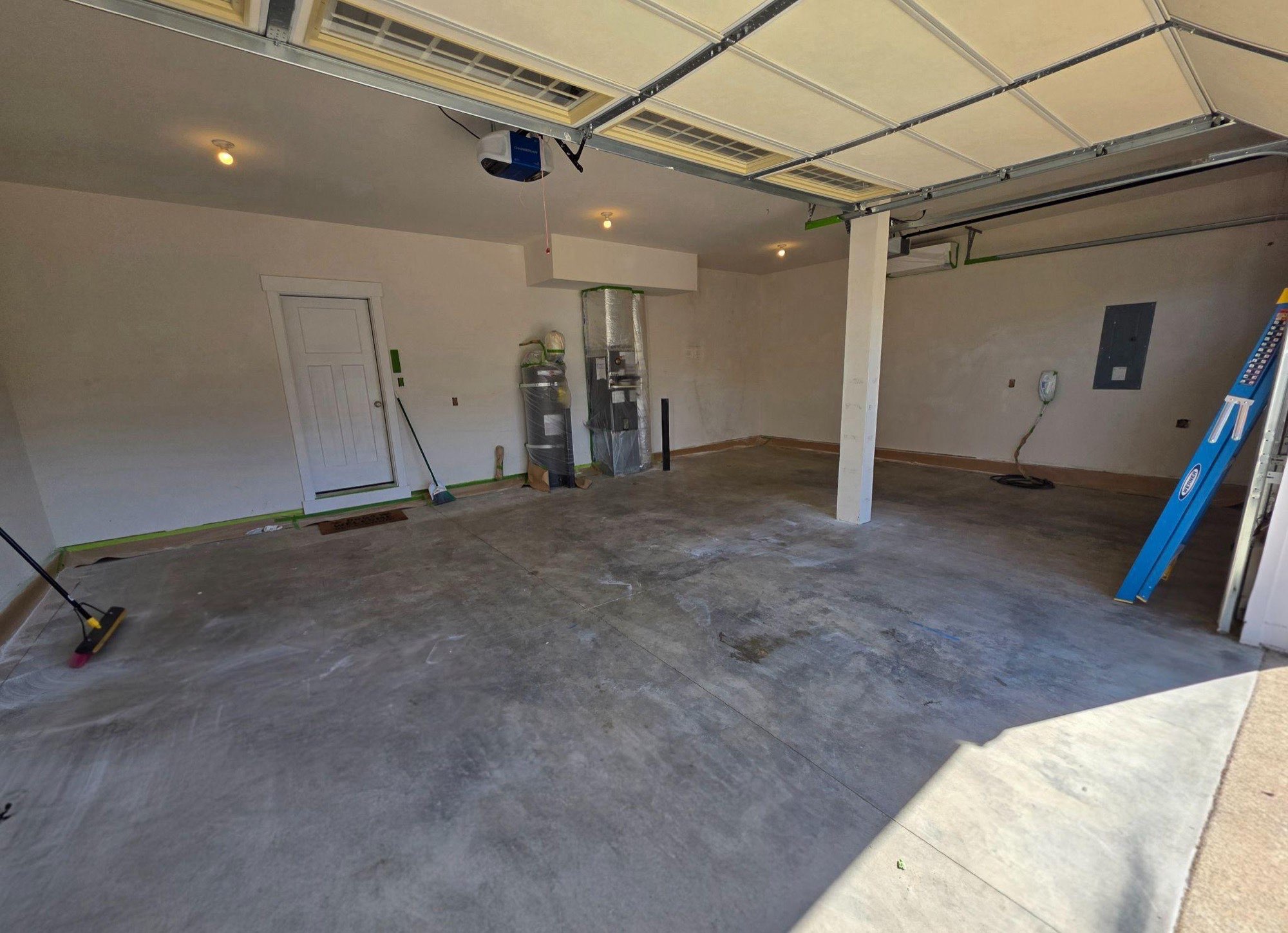 Empty two-car garage with a bare grey concrete slab, cream walls and a ladder standing against the right-hand wall